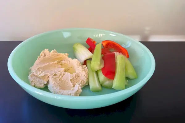 Eine mittelgroße flache Schüssel aus farbigem Glas in Mosser-Optik mit Hummus und Gemüse darin