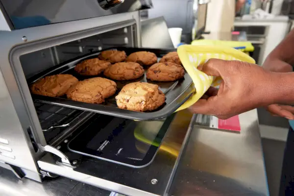 鍋つかみを使って、インスタント ポット オムニ プラス エアフライヤー トースター オーブンから焼き上がったクッキーのシートを手で取り出す