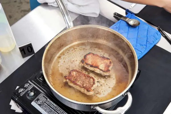 Person, die Fleisch auf einem professionellen 10-teiligen Edelstahl-Kochgeschirrset der Hestan ProBond Collection brät