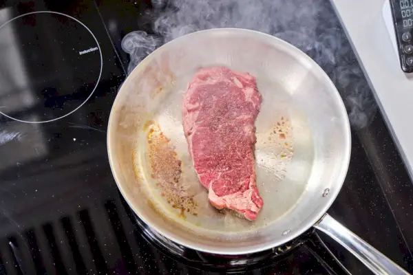 Heben Sie mit der Hand einen Deckel von einem Topf im 10-teiligen Edelstahl-Kochgeschirrset von Le Creuset auf einem Herd.