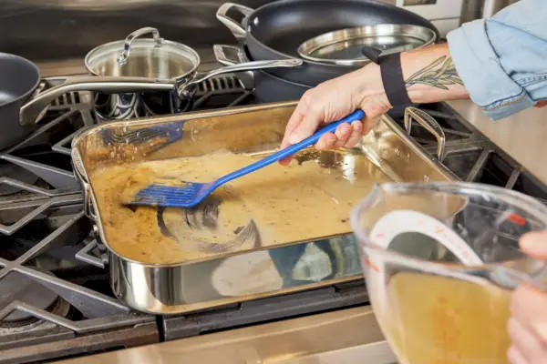 Le Creuset 스테인리스 스틸 로스팅 팬과 붙지 않는 랙이 소스를 만드는 데 사용되고 있습니다.