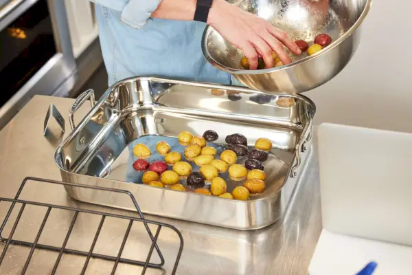 붙지 않는 랙이 있는 Le Creuset 스테인리스 스틸 로스팅 팬에 감자를 넣는 사람