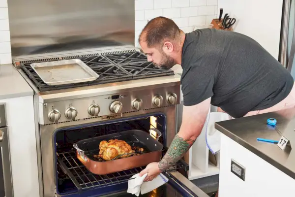 오븐에서 Nordic Ware Copper Turkey Roaster with Rack을 꺼내는 사람