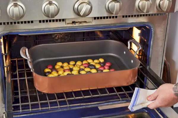 랙이 달린 Nordic Ware 구리 칠면조 로스터가 감자가 담긴 오븐에 놓여 있습니다.