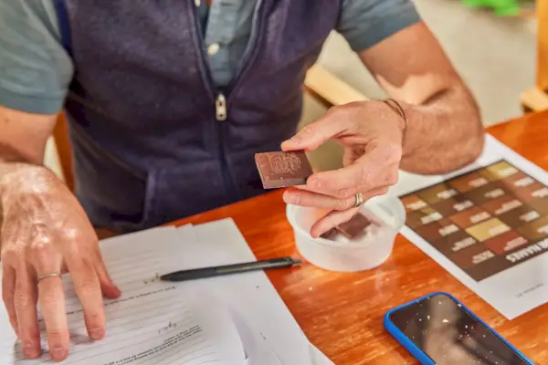 Uma pessoa segurando um pedaço de uma barra de chocolate amargo Theo 85%