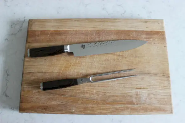 Das Shun Premier Tranchiermesser- und Fleischgabel-Set auf einem Holzschneidebrett