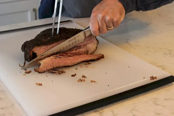 Eine Person schneidet mit dem Messermeister Avanta Kullenschliff Tranchierbesteck Fleisch