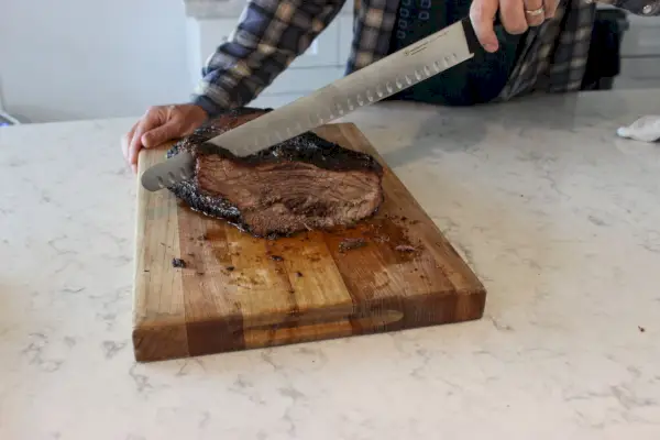 Eine Person schneidet Fleisch mit dem Wüsthof Gourmet 14-Zoll-Brustmesser mit hohler Kante