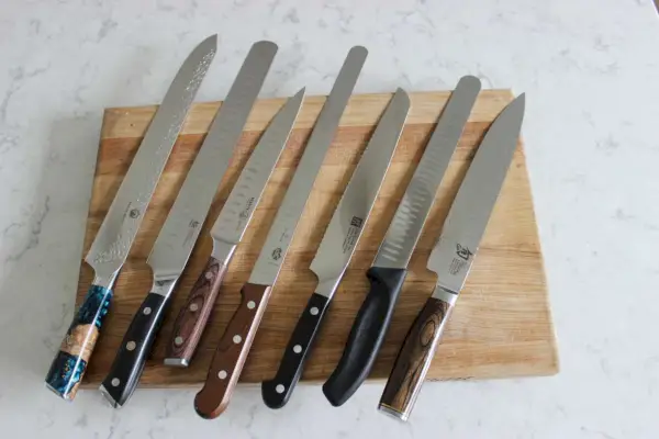 Auf einem Holzschneidebrett sind sieben Brustmesser aufgereiht