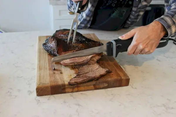 Eine Person verwendet das elektrische Messer von Cuisinart, um Fleisch zu schneiden