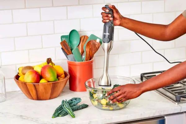 אדם המשתמש בבלנדר טבילה של Breville Control Grip על ירקות בקערה