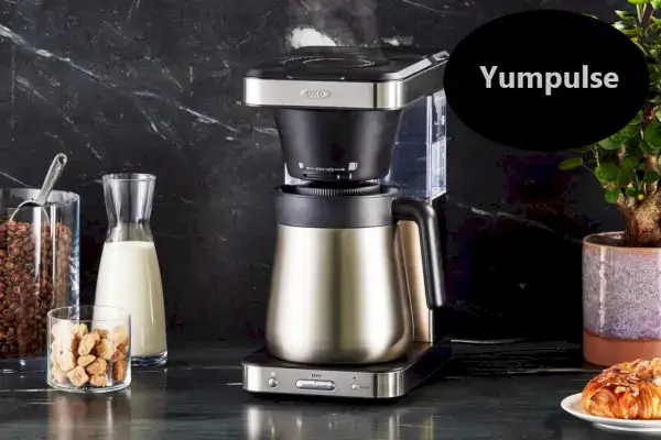 Máquina de café OXO Brew 8 xícaras na bancada cercada por alimentos para o café da manhã com um'Yumpulse' Faves badge overlay