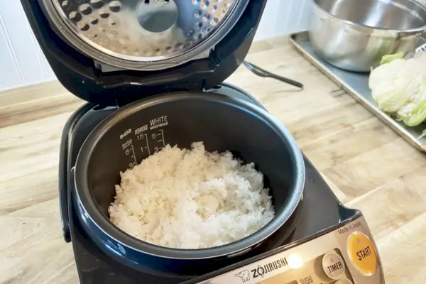 Panela elétrica e aquecedor de arroz com sistema de aquecimento por indução Zojirushi exibido com arroz dentro na superfície de madeira
