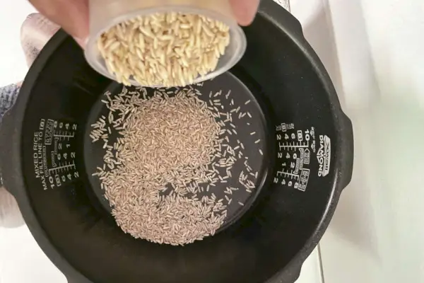Mão derramando arroz na panela de arroz de pressão Cuckoo CRP-P1009SB