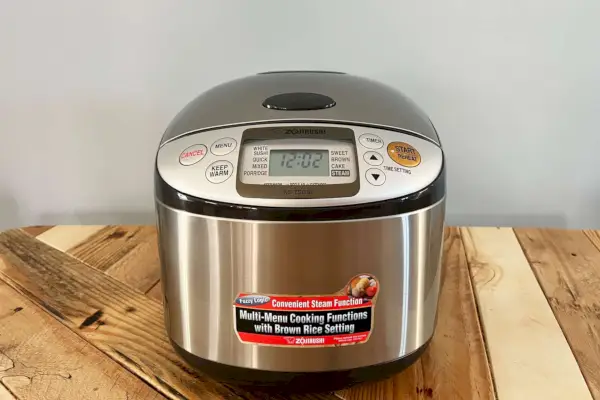 Panela elétrica e aquecedor de arroz Zojirushi NS-TSC18 Micom exibidos em mesa de madeira