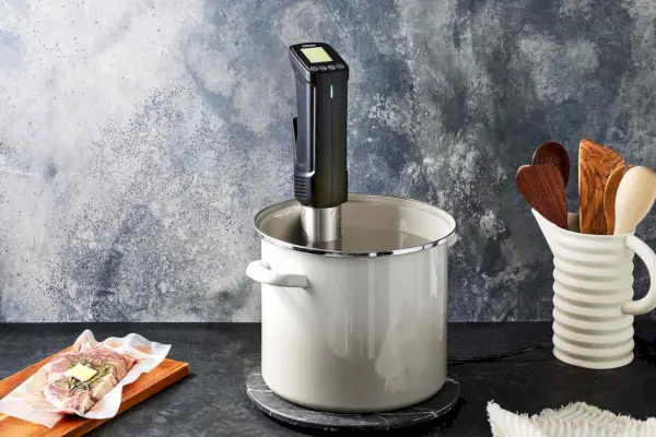 Der Inkbird Sous-Vide-Präzisionskocher ISV-100W ist auf einem Tisch neben dem Vasallenstand und gefrorenem Essen auf einer Holzplatte ausgestellt