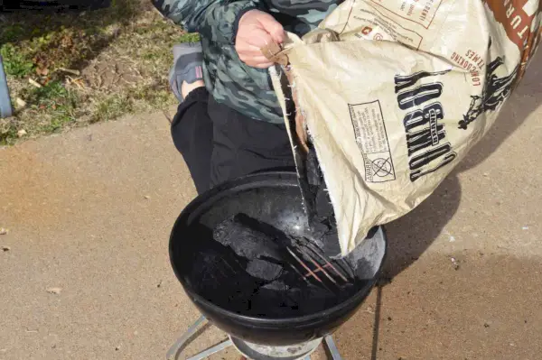 Cowboy All Natural Hardwood Lump Charcoal wird in einen Grill gegeben