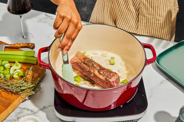 Le Creuset Signature Round Dutch Oven aus emailliertem Gusseisen, 7,25 qt. mit Zutaten auf schwarzer Theke angezeigt