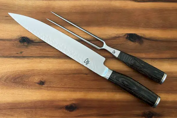 Shun Premier cuchillo para trinchar y tenedor para carne mostrado en una tabla para cortar madera