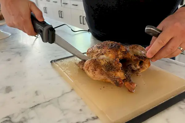 Una persona que usa el cuchillo eléctrico Cuisinart para cortar un pollo.