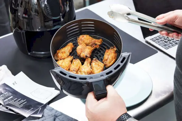 Mano sosteniendo la canasta de la freidora Chefman 3 de 7 cuartos con alitas de pollo cocidas