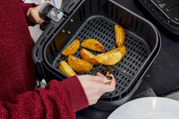 Persona que usa un tenedor para voltear gajos de papa en la freidora de aire Cosori Pro Gen 2