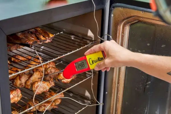 Une personne vérifie la température du poulet en cours de cuisson à l'intérieur du fumoir électrique numérique Masterbuilt de 40 pouces (MB20072918)
