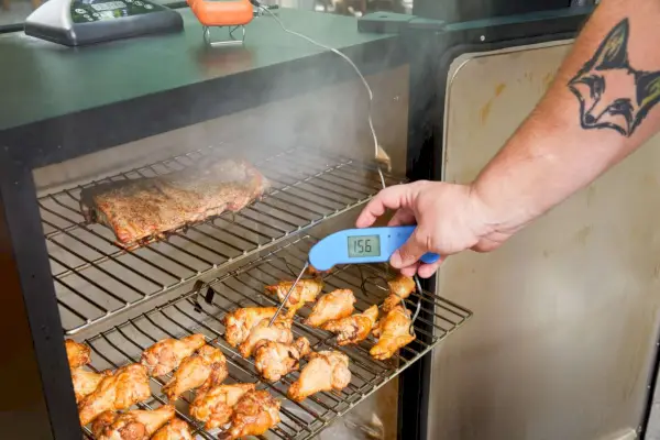 Une personne vérifie la température à l'intérieur des ailes de poulet en cours de cuisson à l'intérieur du fumoir électrique numérique Masterbuilt de 40 pouces (MB20072918)