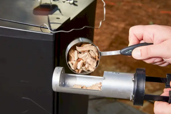 Une personne ramasse des copeaux de bois dans le fumoir électrique numérique Masterbuilt de 40 pouces (MB20072918)