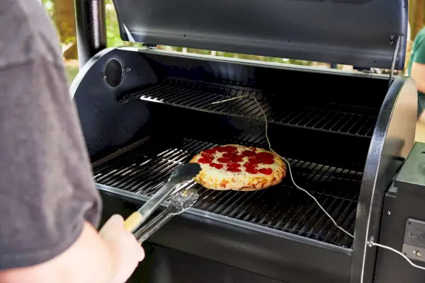 Personne sortant une pizza du gril et fumoir à granulés de bois Traeger Pro Series 780