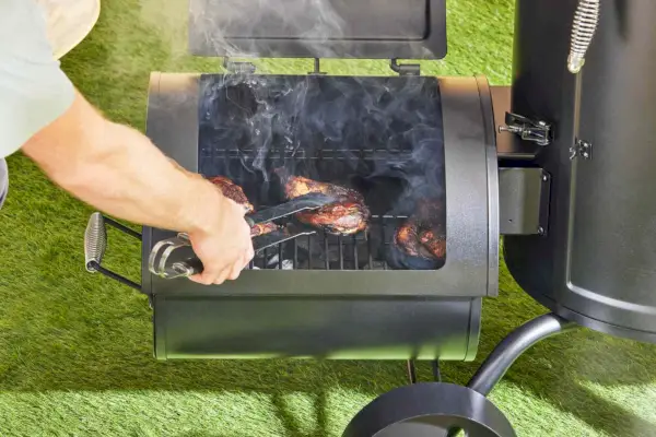 Une personne fait cuire de la viande à l'intérieur du fumoir à charbon vertical décalé de la série Signature Dyna-Glo