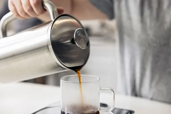 Primer plano de una mano sirviendo café en una taza de la prensa francesa Espro P7