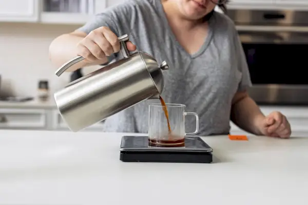 Persona sirviendo café de una prensa francesa Frieling de doble pared en una taza de vidrio en una balanza