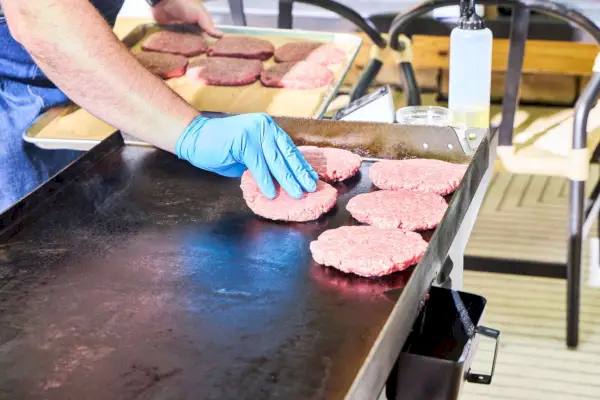 Una persona cocina hamburguesas en la parrilla de gas Blackstone 1554 Cooking de 4 quemadores con parte superior plana
