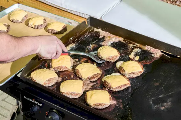 Las hamburguesas con queso se cocinan en la parrilla de gas con superficie plana de 4 quemadores Blackstone 1554 Cooking