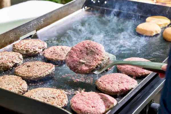La carne de hamburguesa se cocina en la parrilla de gas Blackstone 1554 Cooking de 4 quemadores con parte superior plana