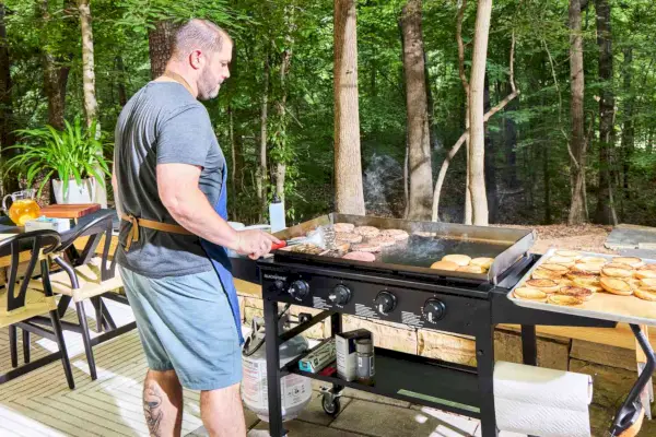 Una persona cocina afuera en la parrilla de gas Blackstone 1554 Cooking de 4 quemadores con parte superior plana