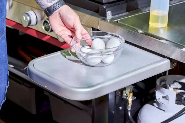 Una persona coloca huevos en la mesa auxiliar Weber Slate 30 Inch Griddle
