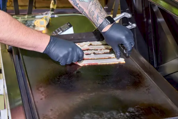 Una persona coloca tocino en la plancha Weber Slate de 30 pulgadas