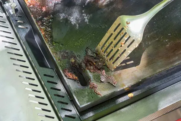 Una persona limpia la parte superior de la plancha Weber Slate de 30 pulgadas con una espátula