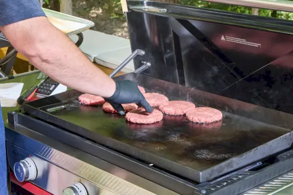 Una persona cocina carne en la plancha Weber Slate de 30 pulgadas