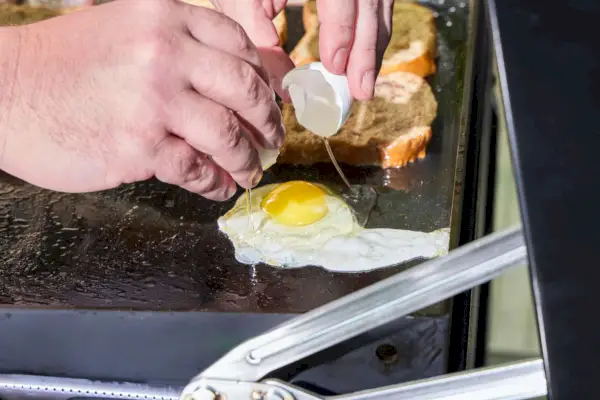 Una persona cocina huevos en la plancha Weber Slate de 30 pulgadas