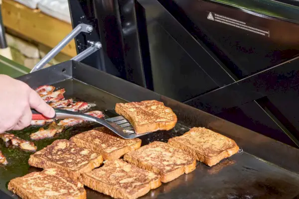 Una persona cocina tostadas francesas y tocino en la plancha Weber Slate de 30 pulgadas
