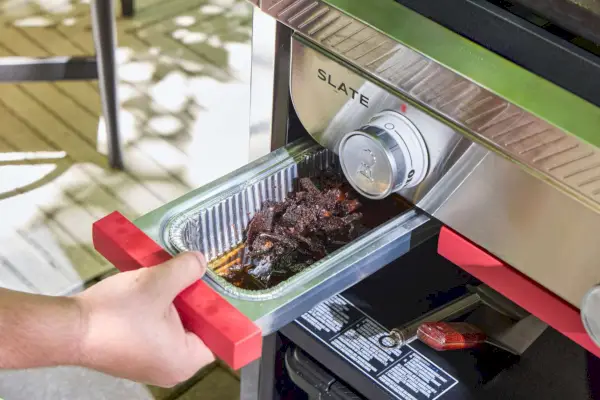 Una persona retira la bandeja de goteo de la plancha Weber Slate de 30 pulgadas