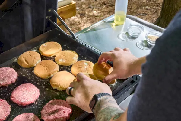 Una persona cocina hamburguesas en la plancha Weber Slate de 30 pulgadas