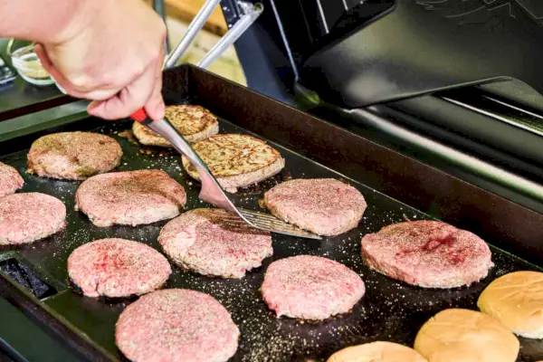 Una persona cocina hamburguesas en Traeger Flatrock Flat Top Grill