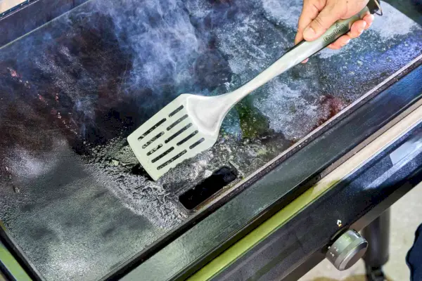 Una persona limpia la parte superior de la parrilla Traeger Flatrock Flat Top con una espátula