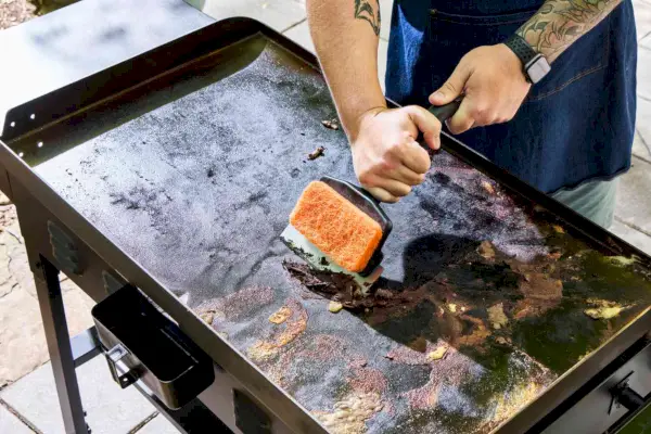 Uma pessoa limpa a churrasqueira a gás Blackstone 1554 Cooking 4 Burner Flat Top