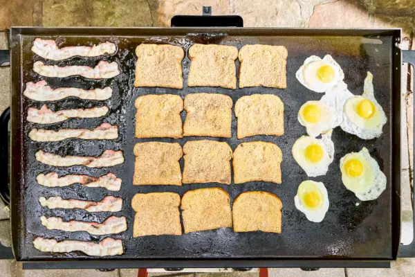 Tocino, tostadas francesas y huevos se cocinan en la parrilla de gas con superficie plana de 4 quemadores Blackstone 1554 Cooking