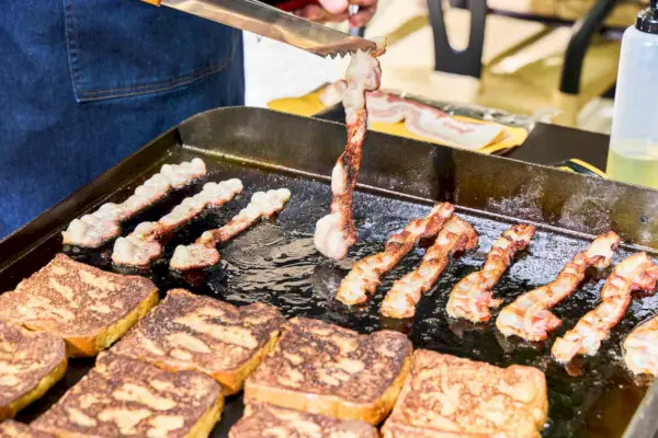 Las tostadas francesas y el tocino se cocinan en la parrilla de gas con tapa plana de 4 quemadores Blackstone 1554 Cooking